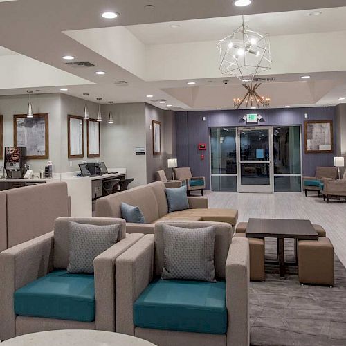 This image shows a modern hotel lobby with comfortable seating, a reception desk, decorative lighting, and large windows near the entrance.