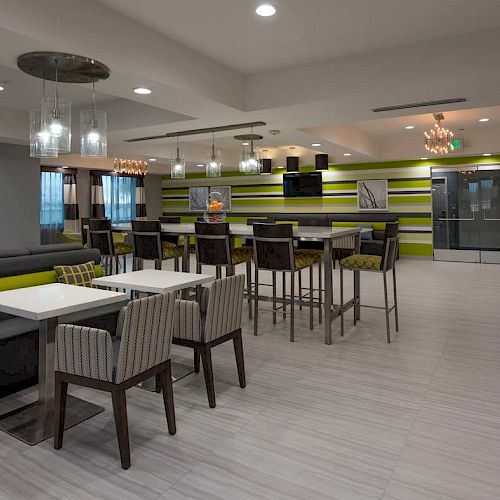 A modern dining area with tables and chairs, bright lighting, a beverage dispenser, and green-striped walls in a spacious, contemporary setting.