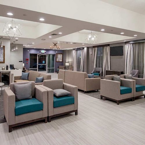 A modern lounge area with comfortable seating, tables, and a kitchenette. The space is well-lit with elegant light fixtures and contemporary decor.