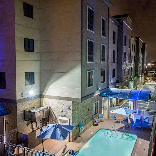 This image shows an outdoor pool area at a hotel at night, with blue lighting accents and several umbrellas and chairs arranged around the pool.