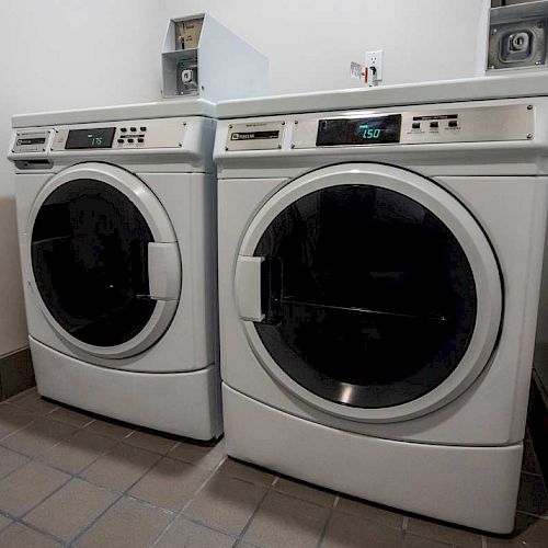 This image shows a laundry room with a washing machine and dryer side by side, against a wall with tiled flooring.