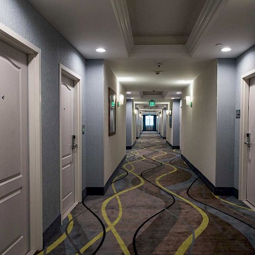 This image shows a hotel hallway with multiple doors on both sides, numbered 314 and 312 visible, and patterned carpet leading to an exit.