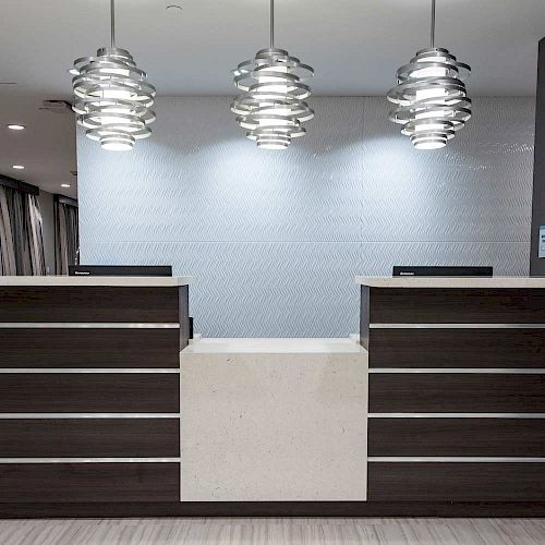 A modern reception desk with two computer monitors and three stylish pendant lights hanging above in a contemporary setting ends the sentence.