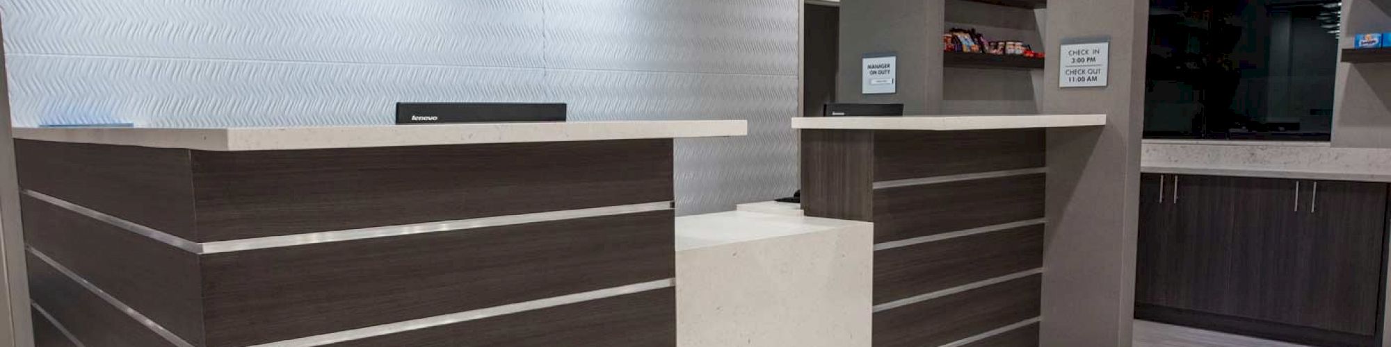 The image shows a modern reception desk area with sleek design, pendant lights above, and a small shelf space in the background.