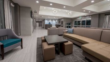 A modern, well-lit lobby with comfortable seating, a table, and a front desk in the background. Minimalist design with neutral tones and elegant decor.