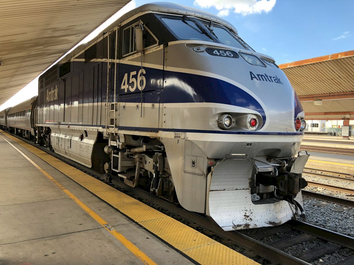 This image shows an Amtrak train, engine number 456, stationary at a platform under a covered station area, with another train car behind it.