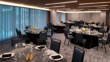 The image shows an elegantly set banquet hall with round tables and chairs, decorated with flowers and candles, ready for a formal event.