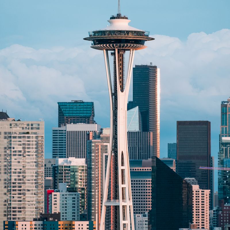 The image features a cityscape with a prominent observation tower, surrounded by modern high-rise buildings and a partly cloudy sky in the background.