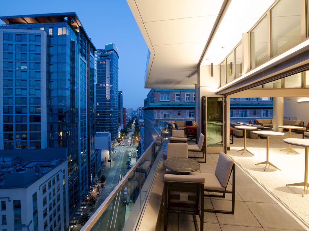 A modern rooftop terrace with seating areas overlooks a cityscape of tall buildings at dusk, featuring a sophisticated urban atmosphere.