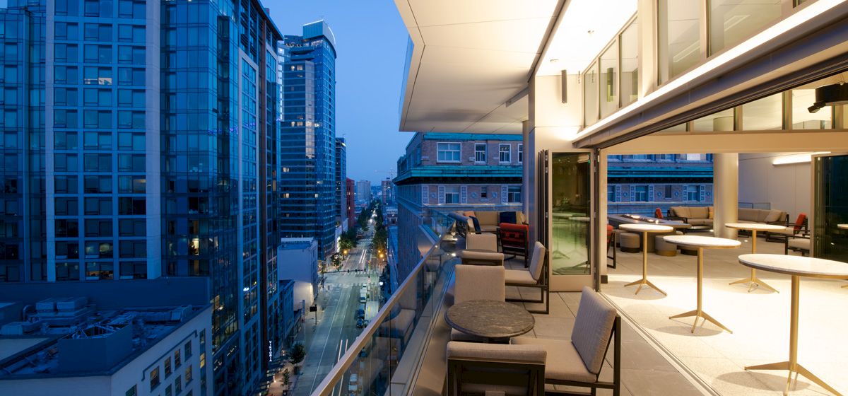 A modern rooftop terrace with seating areas overlooks a cityscape of tall buildings at dusk, featuring a sophisticated urban atmosphere.