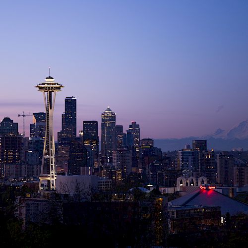 This image shows a twilight view of the Seattle skyline, featuring the Space Needle with Mount Rainier visible in the background.