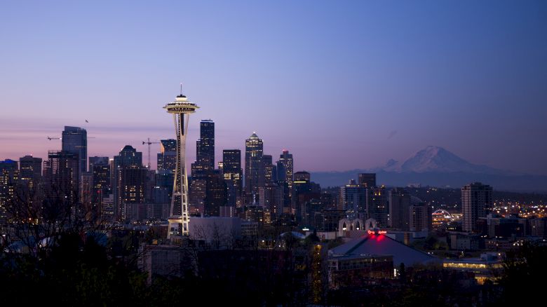 A twilight view of the Seattle skyline featuring the Space Needle, with Mount Rainier in the background and illuminated city buildings around it.