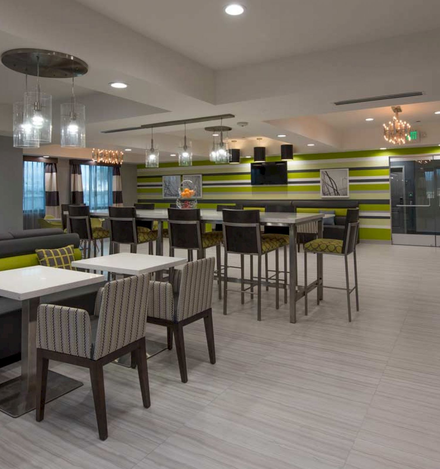 A modern dining area with tables, chairs, a sofa, and a beverage machine, featuring a striped wall design and pendant lighting for ambiance.