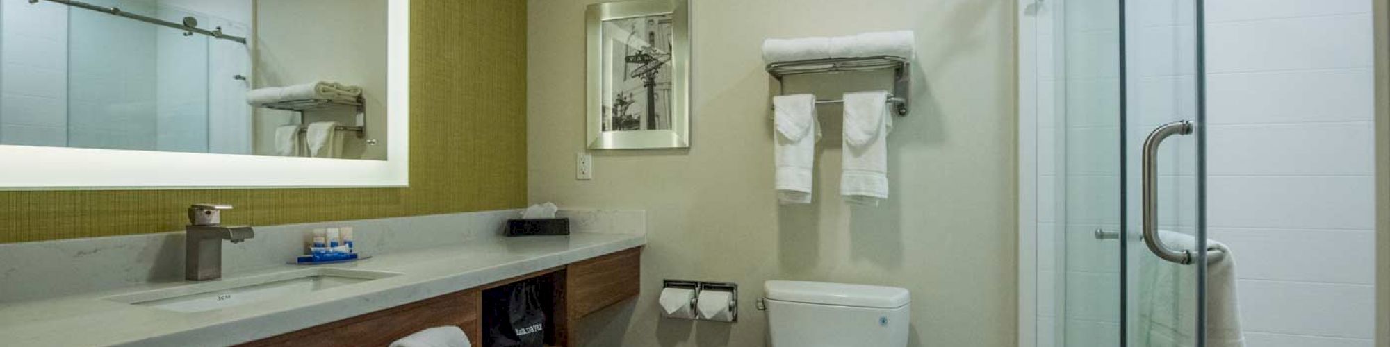 A modern bathroom with a shower, toilet, large mirror, and vanity. Towels are neatly placed on the racks and under the counter.