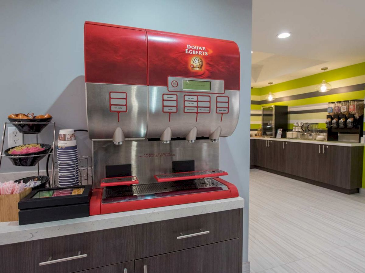 This image shows a self-serve beverage station with dispensers, cups, and condiments in a modern setting, possibly in a hotel or restaurant.